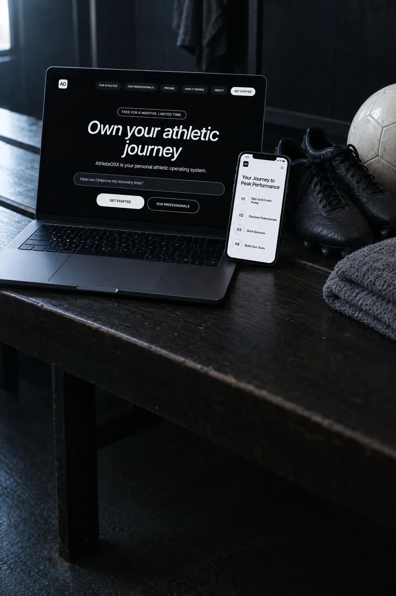 A laptop on a changing-room bench showing the AthleteOSX home page, with a phone showing its how-it-works steps, beside football boots